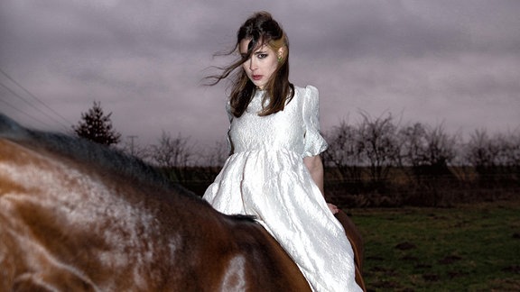 Musikerin BROCKHOFF im silber schimmernden Kleid und zurückgelehnter Pose auf einem Pferd
