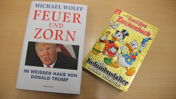 Das Buch "Fire and Fury" und ein Lustiges Taschenbuch mit Donald Duck auf dem Cover liegen nebeneinander auf einem Tisch.