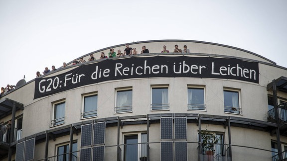 An einer Häuserwand hängt ein Banner mit der Aufschrift "Für die Reichen über Leichen"