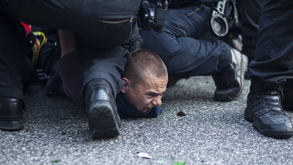 Ein Demonstrant wird von Polizisten auf den Boden gedrückt