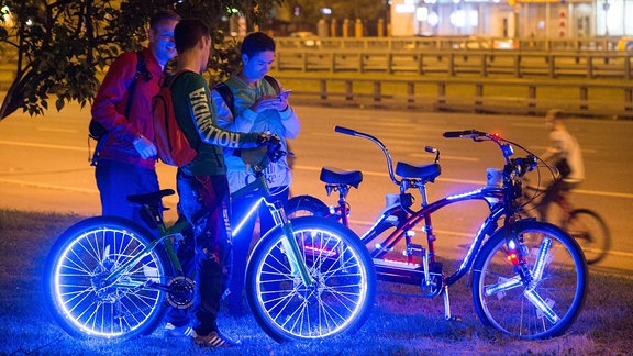 Drei junge Männer mit ihren Fahrrädern und Handys bei Nacht.