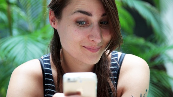Eine junge Frau nutzt ihr Smartphone. Sie zieht dabei eine Augenbraue hoch und schaut auf das Display.