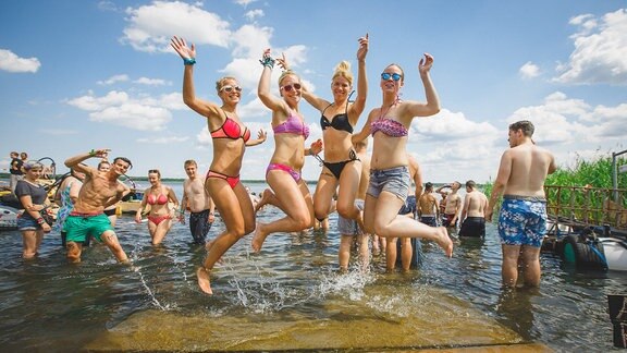 Vier junge Frauen springen aus dem Baggersee auf dem Festivalgelände in Ferropolis.