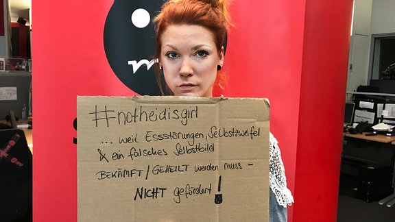 Vanessa hält ein Pappschild mit der Aufschrift "#notheidisgirl, weil Essstörungen, Selbstzweifel und ein falsches Selbstbild bekämpft / geheilt werden muss. Nicht gefördert.
