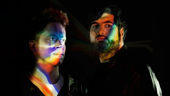 Portraitaufnahme des Duos, auf ihren Gesichtern reflektieren sich die Spektralfarben. (Pressebild)