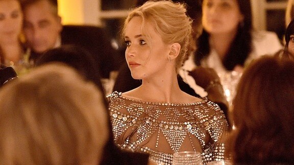 Jennifer während einer Dinnerparty in Pailletten besetztem Abendkleid. Sie sitzt mit mehreren Gästen am Tisch, es herrscht (fast) Kerzenlicht-Atmosphäre. Ihr Blick geht nach links, ihr Haar ist hochgesteckt.