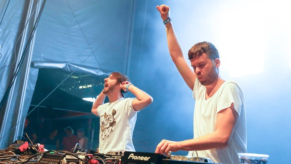 Beide Djs tragen weiße T-shirts hinter dem DJ-Pult und feuern die Fans auf dem Electro-Magnetic-Festival an.