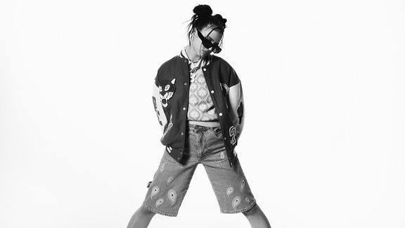 Musikerin Nina Chuba steht breitbeinig da, mit Händen in den Taschen und mit Sonnenbrille, schwarz-weiß Bild