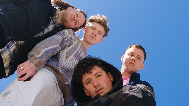 Die vier Bandmitglieder von Provinz schauen von oben nach unten in die Kamera. Im Hintergrund: blauer Himmel.