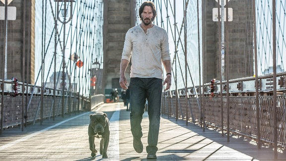 Szene aus John Wick 2, in der der Hauptdarsteller mit einem Hund über eine Brücke läuft.