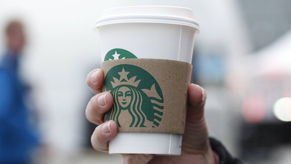 Hand hält einen Starbucks-Becher in der Hand.