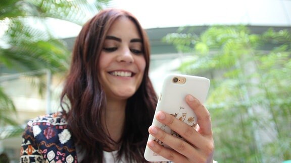 SPUTNIKerin Josy blickt lächelnd auf ihr Smartphone