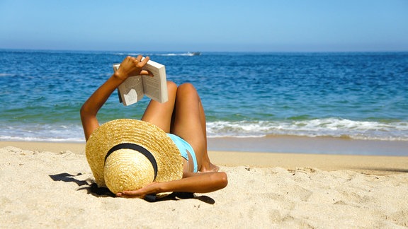 Eine Frau liegt am Strand und liest ein Buch