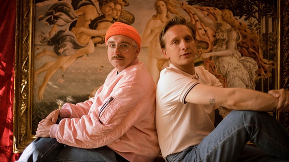 Felix und Steffen sitzen vor einem riesigen Gemälde