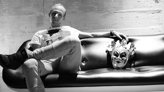 Boris Brechja sitzt auf einer Couch, nehmen ihm liegt eine klassische Karnevalsmaske