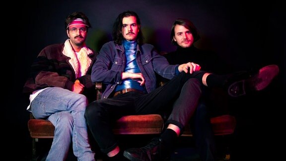 Die drei Künstler der Band "Das Moped" lümmelt auf einem Sofa.