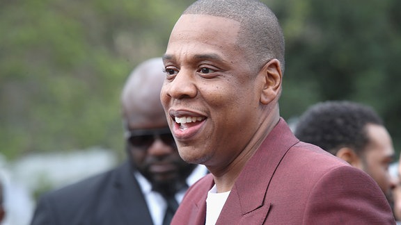 Jay-Z schaut lächelnd in Richtung Reporter.