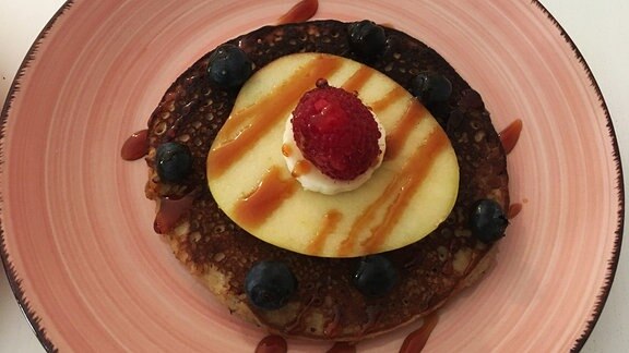 Paleo-Pancakes aus Eiern und Bananen, verziert mit einer Apfelscheibe und einer Himbeere. 