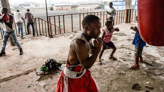 Ein schwarzer Junge trainiert Boxen an einem Sandsack.