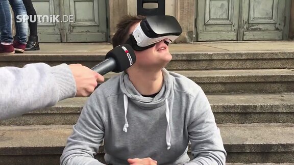 Junger Mann testet eine VR-Brille und spricht dabei in ein SPUTNIK-Mikrofon.